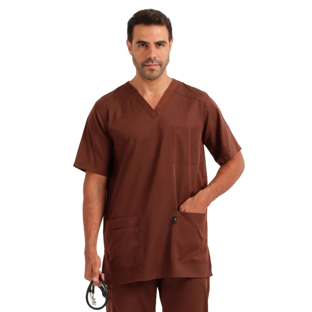 A man modeling a matching brown scrub set consisting of a short-sleeve V-neck top and matching pants, standing against a plain light gray studio background.